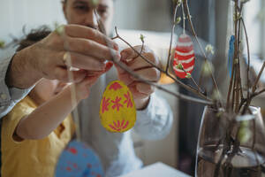 Father and son decorating painted Easter eggs on twigs - ANAF02778