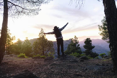 Carefree man standing with arms outstretched near trees - ASGF04941