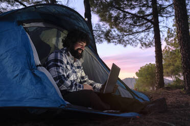 Lächelnder Freiberufler arbeitet am Laptop im Zelt - ASGF04945