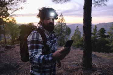Man wearing headlamp and using smart phone at sunset - ASGF04951