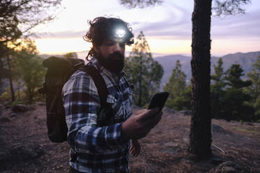 Mann mit Stirnlampe und Smartphone bei Sonnenuntergang - ASGF04951