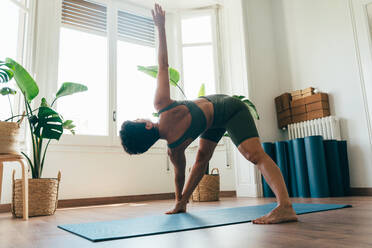 Beautiful sporty girl making yoga training in the gym studio. Young woman coach with short hair performing yoga and acroyoga poses, warming up for the class. Concepts of healthy lifestyle and sport disciplines - DMDF10872