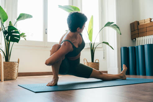 Beautiful sporty girl making yoga training in the gym studio. Young woman coach with short hair performing yoga and acroyoga poses, warming up for the class. Concepts of healthy lifestyle and sport disciplines - DMDF10874