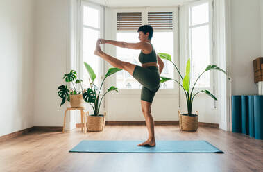 Beautiful sporty girl making yoga training in the gym studio. Young woman coach with short hair performing yoga and acroyoga poses, warming up for the class. Concepts of healthy lifestyle and sport disciplines - DMDF10892