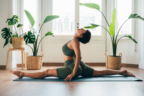 Beautiful sporty girl making yoga training in the gym studio. Young woman coach with short hair performing yoga and acroyoga poses, warming up for the class. Concepts of healthy lifestyle and sport disciplines - DMDF10901