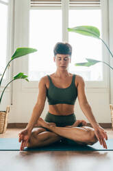 Beautiful sporty girl making yoga training in the gym studio. Young woman coach with short hair performing yoga and acroyoga poses, warming up for the class. Concepts of healthy lifestyle and sport disciplines - DMDF10924