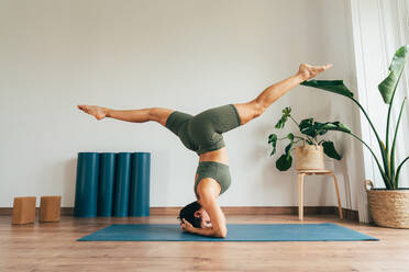 Beautiful sporty girl making yoga training in the gym studio. Young woman coach with short hair performing yoga and acroyoga poses, warming up for the class. Concepts of healthy lifestyle and sport disciplines - DMDF10956