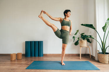 Beautiful sporty girl making yoga training in the gym studio. Young woman coach with short hair performing yoga and acroyoga poses, warming up for the class. Concepts of healthy lifestyle and sport disciplines - DMDF10957