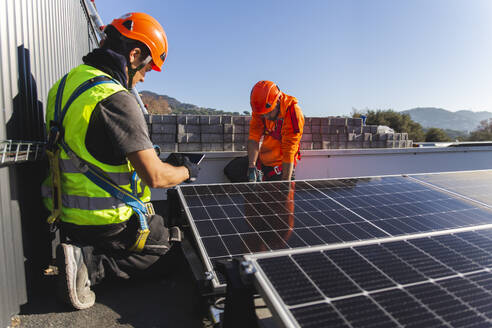 Two technicians installing solar panel on rooftop - PCLF00982