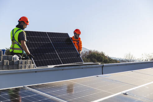 Two engineers installing solar panel on rooftop - PCLF00984