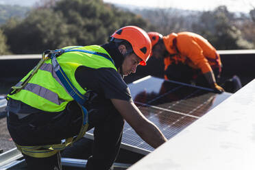 Techniker bei der Installation eines Solarpanels mit einem Mitarbeiter auf dem Dach - PCLF00987