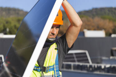 Älterer Arbeiter trägt Solarmodul an einem sonnigen Tag - PCLF00989