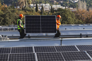 Mitarbeiter tragen Solarpanel auf das Dach - PCLF00993