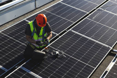 Älterer Techniker mit Drohne, die auf einem Solarpanel sitzt - PCLF00997