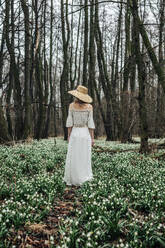 Woman wearing white dress and standing amidst Lily-of-the-valley flowers in forest - VSNF01731