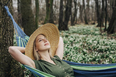 Unbekümmerte Frau mit geschlossenen Augen entspannt sich in einer Hängematte im Wald - VSNF01737