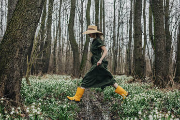 Woman crossing over creek amidst Lily-of-the-valley flowers in forest - VSNF01738