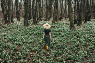 Frau mit Weidenhut und Spaziergang inmitten von Maiglöckchenblüten im Wald - VSNF01739