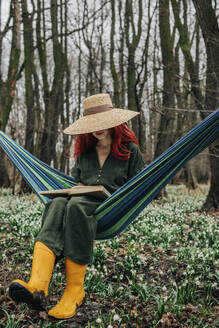 Frau liest Buch in der Nähe von Maiglöckchenblüten im Wald - VSNF01744