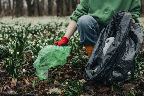 Frau sammelt Plastikmüll in der Nähe von Maiglöckchenblüten im Wald - VSNF01748