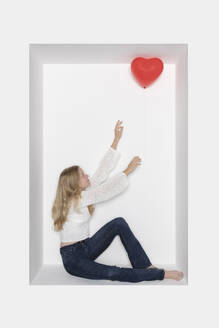 Teenager-Mädchen mit herzförmigem Ballon in einer Nische sitzend - PSTF01093