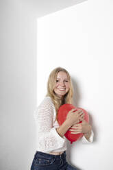 Smiling teenage girl with heart shape balloon against white background - PSTF01097