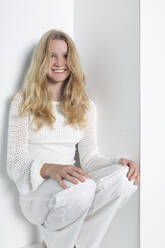 Smiling teenage girl squatting against white background - PSTF01112