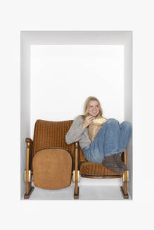 Teenager having popcorn sitting on chairs in alcove - PSTF01128