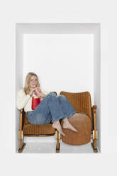 Teenage girl drinking juice sitting on chairs in alcove - PSTF01130