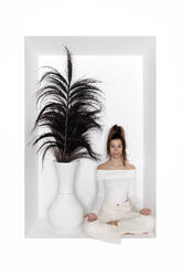 Teenager-Mädchen meditiert Yoga neben einer Vase in einer Nische sitzend - PSTF01151
