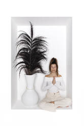 Teenager-Mädchen übt Yoga sitzend neben einer Vase in einer Nische - PSTF01152