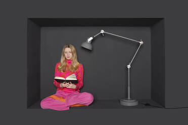 Teenage girl reading book by electric lamp over black background - PSTF01228