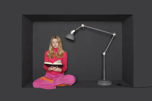 Teenager-Mädchen liest Buch mit elektrischer Lampe auf schwarzem Hintergrund - PSTF01228