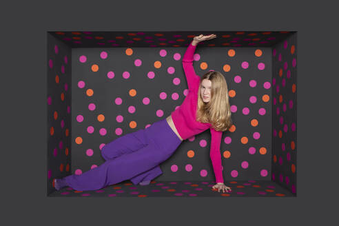 Blond teenager touching alcove against black background with colored dots - PSTF01257