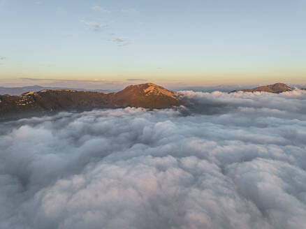 Aerial view of mountain range surrounded by low clouds at sunset as seen from the plane, Salerno, Campania, Italy. - AAEF27706