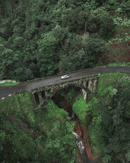 Aerial drone view of a car crossing an old bridge on Madeira island, Portugal. - AAEF27746