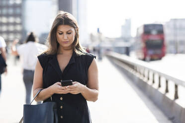 Junge Frau benutzt ein Smartphone auf der Straße in London - WPEF08565