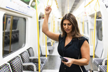 Junge Frau benutzt Mobiltelefon in der U-Bahn - WPEF08578