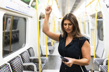 Young woman using mobile phone in subway train - WPEF08578