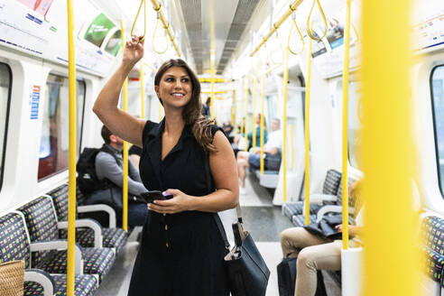 Glückliche junge Frau steht mit Smartphone in der U-Bahn - WPEF08586