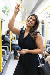 Smiling young woman standing with mobile phone in train - WPEF08588