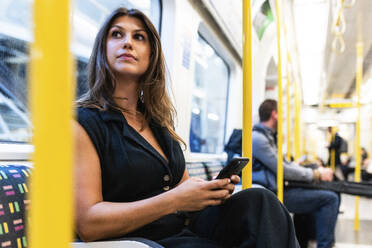 Young woman sitting with smart phone in train - WPEF08589