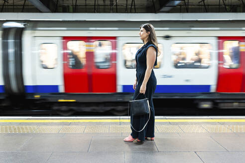 Frau hält Handtasche und steht in der Nähe eines fahrenden U-Bahn-Zuges - WPEF08597