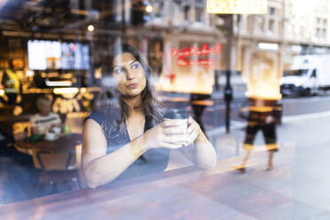 Sitzende Frau mit Kaffeetasse durch Glas gesehen - WPEF08603