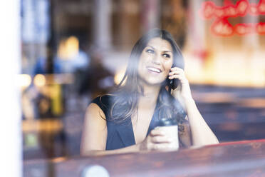 Glückliche Frau, die mit ihrem Smartphone telefoniert und mit einer Kaffeetasse im Café sitzt - WPEF08606