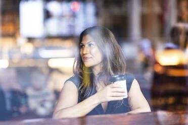 Lächelnde Frau mit Kaffeetasse sitzend und durch Glas gesehen - WPEF08611