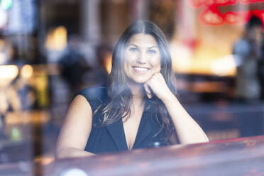 Happy woman sitting in cafe seen through glass - WPEF08614