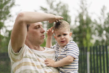 Vater berührt Kopf des weinenden Sohnes im Hinterhof - SEAF02249