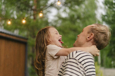 Playful father carrying happy daughter in back yard - SEAF02252