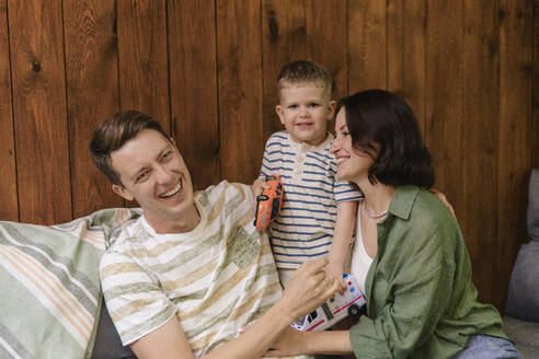 Happy parents with son holding toys on sofa at home - SEAF02260